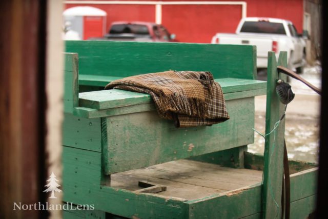 A folded wool blanket rests on the seat of a green wagon at The Kingdom’s Horse Drawn Wagon and Sleigh Rides in Brownington, waiting for a group of riders. (Photo by Tim Lenahan)