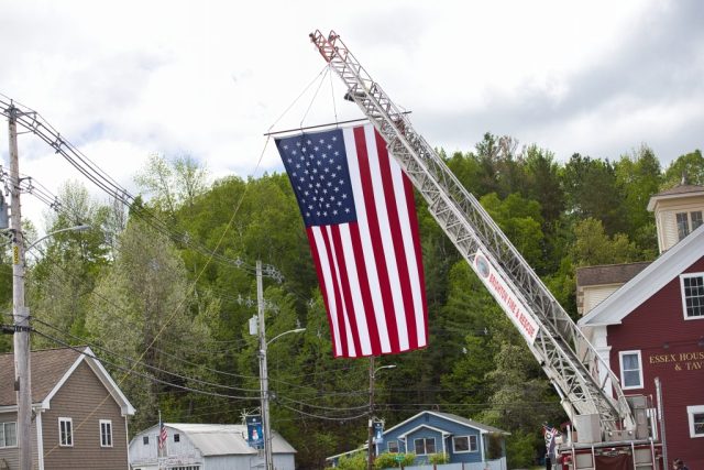 4G0A9337 Large American flag suspended from a Brighton Fire & Rescue ladder truck as veterans march in the Island Pond Memorial Day parade.