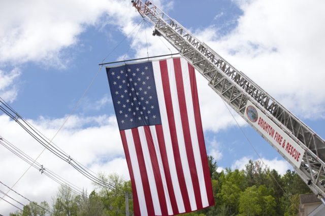 4G0A9340 Large American flag suspended from a Brighton Fire & Rescue ladder truck as veterans march in the Island Pond Memorial Day parade.