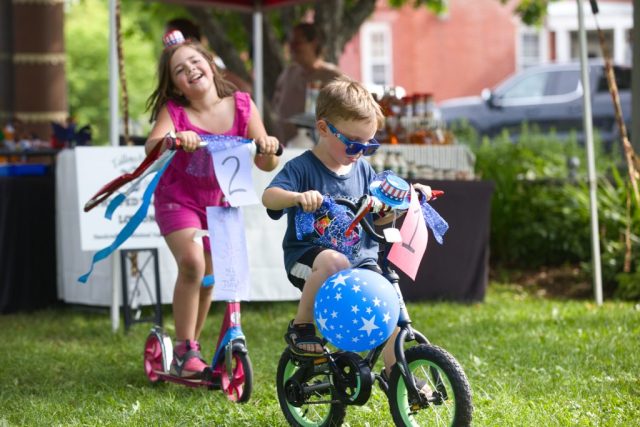 4G0A3473 Two children ride a decorated bicycle and scooter during the patriotic children’s parade at the Danville Farmers Market in Danville, Vermont.