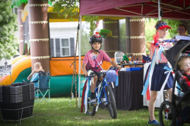 4G0A3507 A boy rides a bicycle decorated with American flags and red, white and blue streamers during the children’s patriotic parade at the Danville Farmers Market in Danville, Vermont.