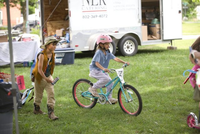4G0A3518 A girl rides her bicycle beside a child in cowboy attire during the patriotic children’s parade at the Danville Farmers Market in Danville, Vermont.