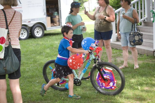 4G0A3531 A boy pushes his bicycle decorated with patriotic balloons, streamers and red, white and blue decorations during the children’s parade at the Danville Farmers Market in Danville, Vermont.